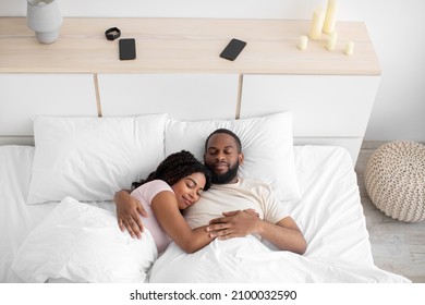 Calm millennial african american female and male sleeping at night, hugging on bed in bedroom interior, free space. Relaxation and healthy sleep together at weekend, love and relationships, top view