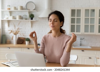 Calm millennial Caucasian female sit at desk at home office work on laptop meditate with mudra hands. Young woman distracted from computer job practice yoga breathe fresh air. Peace concept.