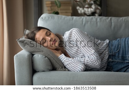 Calm millennial Caucasian woman lying relaxing on couch in living room sleeping taking nap. Tired exhausted young female rest on sofa at home daydream relieving negative emotions. Stress free concept.