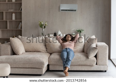 Calm millennial Latino woman lying relaxing on couch in living room breathe fresh ventilated condition air. Happy young Hispanic female renter rest on sofa at home relieve negative emotions.