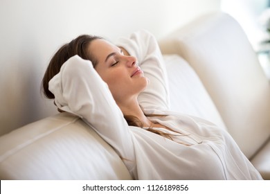Calm millennial woman relaxing on soft comfortable sofa meditating or having daytime nap, carefree lazy girl breathing fresh air enjoying no stress free peaceful weekend morning resting on couch