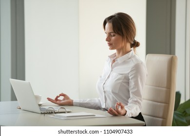 Calm mindful businesswoman meditating at office desk with eyes closed, female executive practicing yoga at workplace enjoying mental emotional mind balance reducing no work stress free relief concept