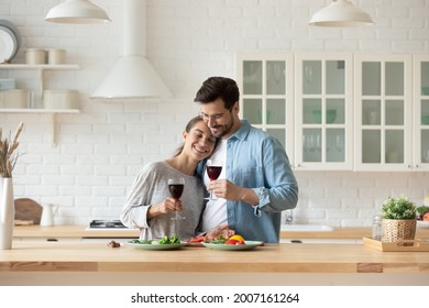 Calm Mixed-race Spouses Hugging In Kitchen With Wine Glasses. Couple Celebrate Anniversary, Special Occasion, Enjoy Dating Together At Home. Romantic Relations, St. Valentines Day Celebrations Concept