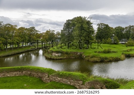 A calm moat surrounded by trees and green grass near the historic Kuressaare Castle in Saaremaa, Estonia.