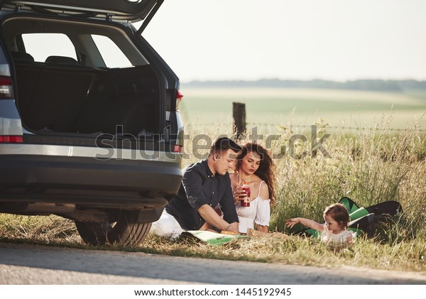 Calm mood. Family have picnic at countryside near\
silver automobile at\
sunset.