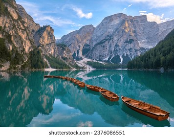 A calm morning by the clear lake Lago di Braies in the Italian Dolomites. The reflection of the mountains on the surface and the foreground with a row of wooden boats creates a great atmosphere.    - Powered by Shutterstock