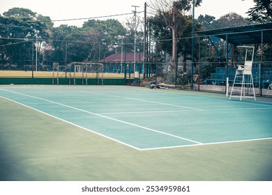 A calm morning scene at a tennis court, with soft sunlight casting gentle shadows on the clean court surface - Powered by Shutterstock