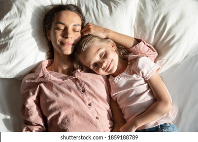 Calm mother with little 6s 7s daughter sleeping together lying down on pillow in comfortable bed, caring mom and lovely kid, top above view. Healthy nap at daytime, repose, relaxation moment concept
