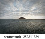 A calm ocean with a distant island under a partly cloudy sky.