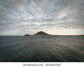 A calm ocean with a distant island under a partly cloudy sky. - Powered by Shutterstock