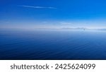 Calm ocean expanse under a hazy sky, with subtle cloud streaks and a distant horizon merging sea with air.