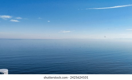 Calm ocean expanse under a hazy sky, with subtle cloud streaks and a distant horizon merging sea with air. - Powered by Shutterstock