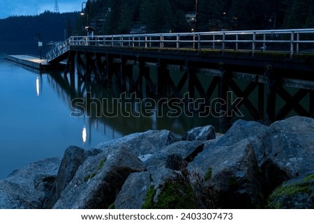 A calm ocean pier at slack tide during the early morning at blue hour, looking out over a tree-lined harbor