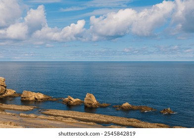 Calm ocean scene with unique coastal rock formations under a vibrant blue sky dotted with white clouds, evoking a sense of tranquility and natural beauty
 - Powered by Shutterstock