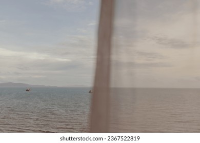 Calm ocean view through thin white curtain in summer.