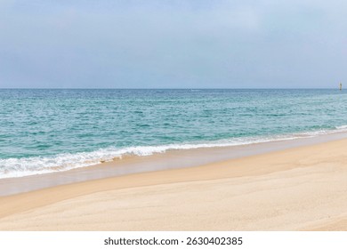 Calm ocean waves gently lapping onto a sandy beach on a clear day with blue skies and distant horizon