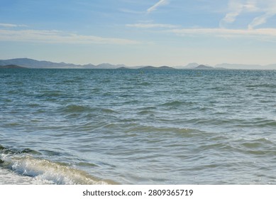Calm ocean waves gently lapping on a sandy beach with distant mountains