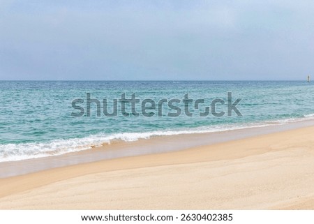 Calm ocean waves gently lapping onto a sandy beach on a clear day with blue skies and distant horizon