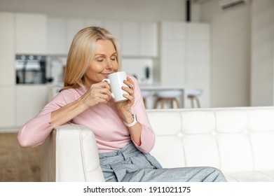 A Calm And Peaceful Middle-aged Woman Takes A Break, Rests With A Cup Of Hot Tea On The Couch At Home. Contented Charming Mature Lady Enjoying Coffee And Daydreaming