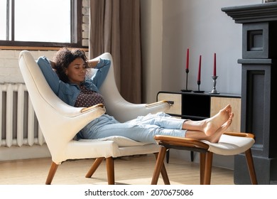 Calm peaceful young African woman taking deep breath of fresh air, reloading mind, resting with closed eyes in soft white armchair. Girl relaxing at home, practicing stress relief techniques - Powered by Shutterstock