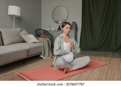 Calm Pregnant Woman Deep Breathing Doing Yoga In Lotus Pose Comfortable At Home.