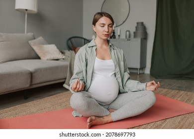 Calm Pregnant Woman Deep Breathing Doing Yoga In Lotus Pose Comfortable At Home.