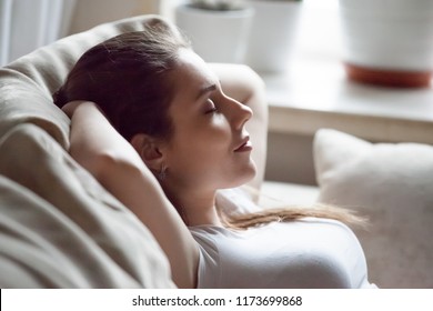 Calm Pretty Millennial Woman Lying On Cozy Sofa Relaxing On Weekend, Peaceful Female Rest With Eyes Closed Hands Over Head On Couch, Happy Girl Taking Nap Or Chilling At Home, Sleep Tired After Work