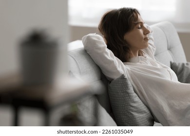 Calm pretty young woman resting on cozy sofa, leaning on soft back with closed eyes, enjoying leisure, break, sleeping, feeling comfortable at cozy home. Candid side portrait - Shutterstock ID 2261035049