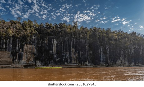 A calm red-brown African river. The forest grows on steep limestone coastal cliffs. Blue sky, clouds. Madagascar. Manambolo River - Powered by Shutterstock