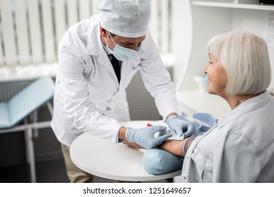 Calm relaxed elderly lady kindly smiling while sitting at the table with her arm straight during the blood collection procedure