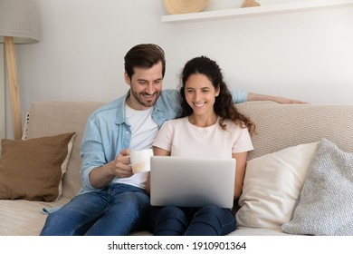 Calm Relaxed Millennial Couple Spend Free Evening Weekend On Cozy Sofa Drink Tea Coffee Watch Movie Using Laptop. Smiling Young Husband Wife Engaged In Choosing Goods At Web Store Chat With Friends