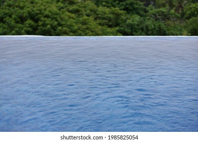 Calm And Relaxing Blue Water Flat Surface Of Infinity Pool With Trees Foliage In Background. For Tourism Luxury Lifestyle Vacation Concept. No People.