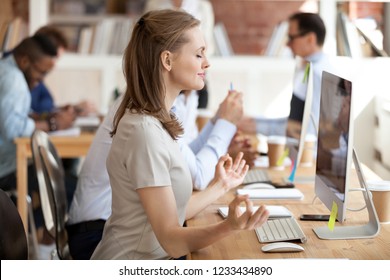 Calm relaxing businesswoman doing yoga exercise, meditating at workplace in front of computer, resting after long work, no stress, breathing deeply, relief, taking break, pause, healthy good habits