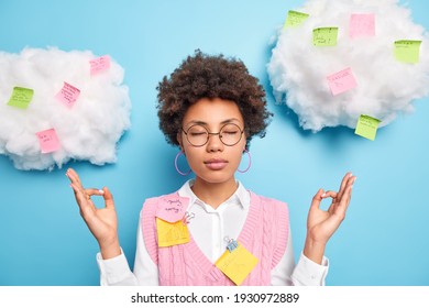 Calm relaxing female office worker feels relieved and stress free meditates indoor keeps eyes closed surrounded with colorful sticky notes takes break from work for mental balance avoids stressful job
