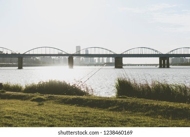 A Calm River And An Arch Bridge And Two Fishing Rods And Green Grass And Blue Sky At Hangang Park, Seoul, South Korea