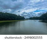 A calm river reflecting a blue sky with scattered dark clouds, surrounded by lush green trees. Several docks stick out from the sides of the riverbank.