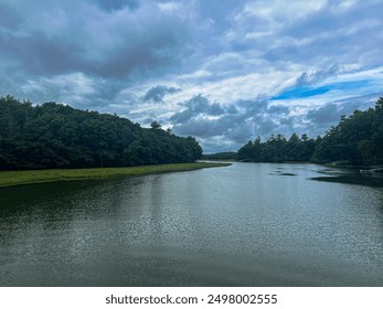 A calm river reflecting a blue sky with scattered dark clouds, surrounded by lush green trees. Several docks stick out from the sides of the riverbank. - Powered by Shutterstock