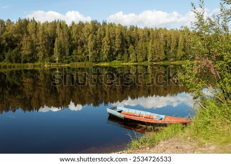 Calm river with trees reflected in the water. Old wooden boat on the river bank. Shuya River in Karelia, Russia
