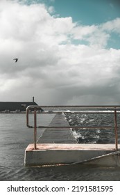 A Calm And Rough Sea With A Centred Wooden Walkway. A Bird Fighting The Wind In The Cloudy Blue Sky.