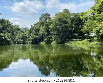 A calm and scenic lakeside view within the campus of Institut Pertanian Bogor (IPB), featuring the Graduate School sign surrounded by lush tropical trees.