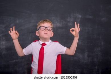 Calm School Boy Meditating Against Blackboard In Class. Child In Yoga Pose. Confidant And Health Breathing. Relaxed Kid In Uniform. Back To School.