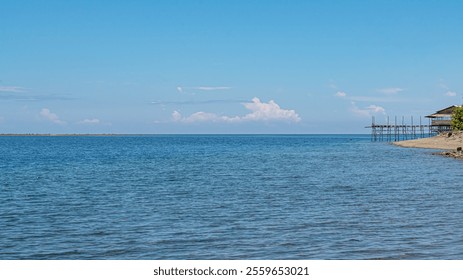 calm seascape with clear blue water, a distant horizon, and a wooden pier. - Powered by Shutterstock