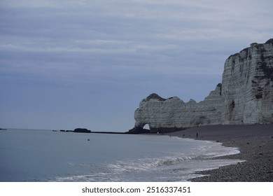 A calm seaside view with towering white cliffs and a pebble beach stretching into the distance - Powered by Shutterstock