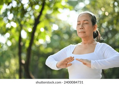 Calm senior woman with eyes closed meditating or practicing traditional Tai Chi Chuan in nature. - Powered by Shutterstock