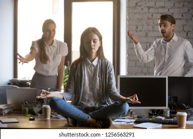 Calm serene employee meditating in office ignoring not listening to annoying colleagues, funny female young worker doing yoga avoiding stress at work for mental balance emotional control concept