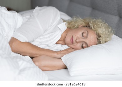 Calm serene sleepy blonde senior woman lying on side, resting on comfortable bed mattress, enjoying relaxation, recreation in morning, sleeping in white linen with head on pillow - Powered by Shutterstock