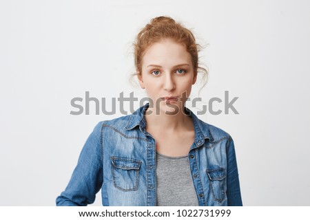Calm serious caucasian ginger girl with hair combed in bun, expressing irritation or indifference while standing over gray background. Sister do not like shopping with friend cause it is boring