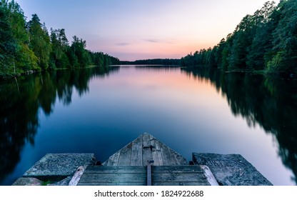 A calm and silent evening at sunset at a small forest lake in Sweden. In the foreground there is a wooden bridge. The lake is surrounded by trees that are reflected in the water - Powered by Shutterstock