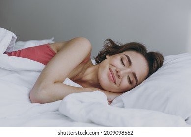 Calm Sleeping Caucasian Happy Young Woman 20s Wear Pajamas Tank Shirt Lying In Bed Lies Wrap Covered Under Blanket Duvet On Pillow Rest Relax Indoors At Home. Good Mood Night Morning Bedtime Concept.