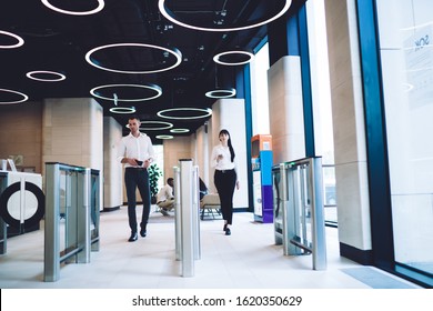 Calm smart colleagues in trendy formal wear going through automatic turnstile gates in hall of light modern building in downtown